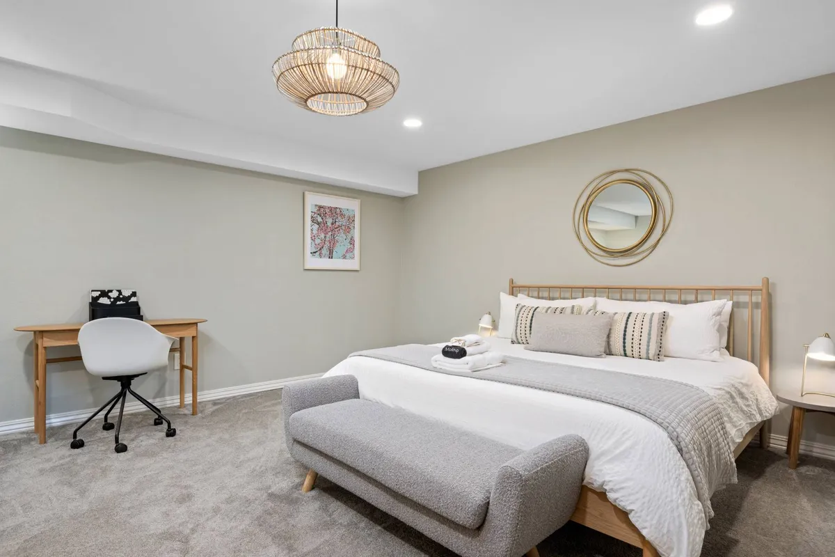 A king bedroom with a bed featuring decorative pillows and a cozy blanket, a round mirror on the wall, and a wooden desk with a chair—offering both relaxation and workspace options within the suite.