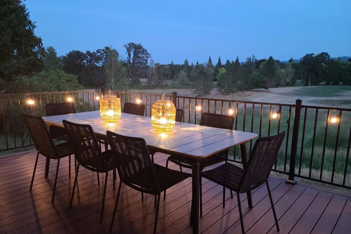 A charming outdoor dining setup with a long table, woven lanterns, string lights, and surrounding landscape. The image exudes warmth and togetherness, ideal for evening meals or stargazing with friends, capturing the spirit of shared experiences.