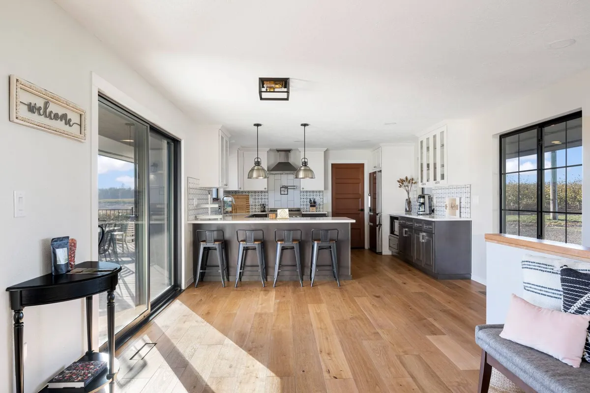 A bright and inviting kitchen area with a large island surrounded by bar stools, set against a backdrop of expansive windows and an open layout leading into the living space. The design encourages both cooking and socializing.