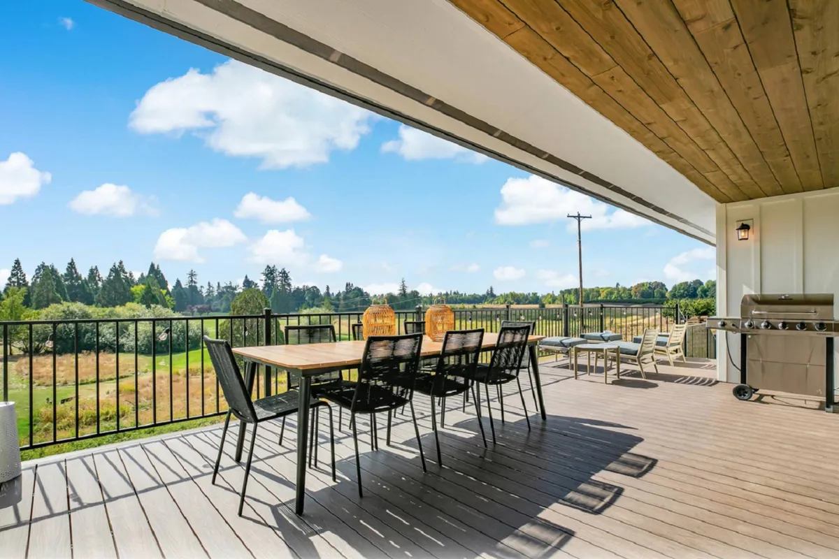 The image captures an inviting outdoor dining area overlooking a sweeping landscape view, complete with a dining table, chairs, and a grill. The scene suggests opportunities for sunset dinners, morning coffee, and relaxed social gatherings, all framed by the natural beauty of the Bayou Golf Course.