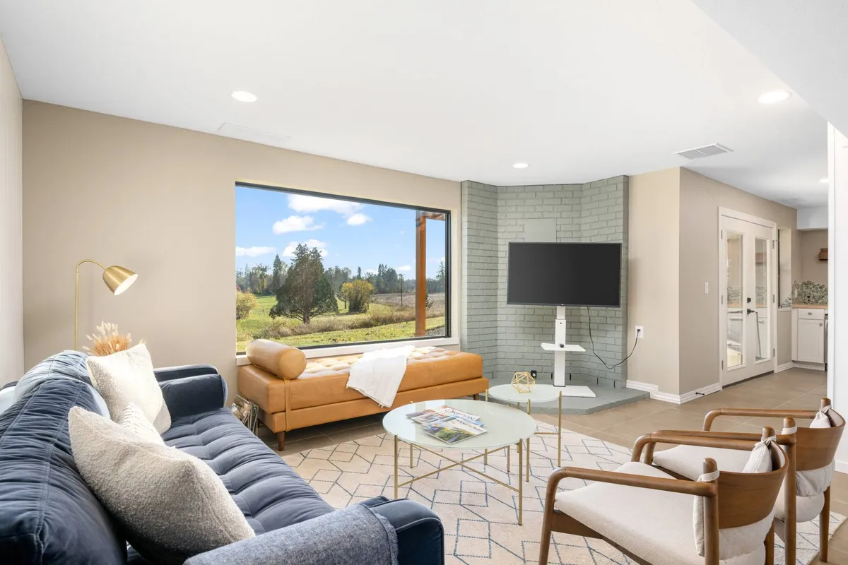 A contemporary living room arranged around a sofa and coffee table, oriented to take advantage of the large window offering scenic views. Soft lighting and comfortable furnishings create an inviting space to relax and enjoy the outdoors from within.