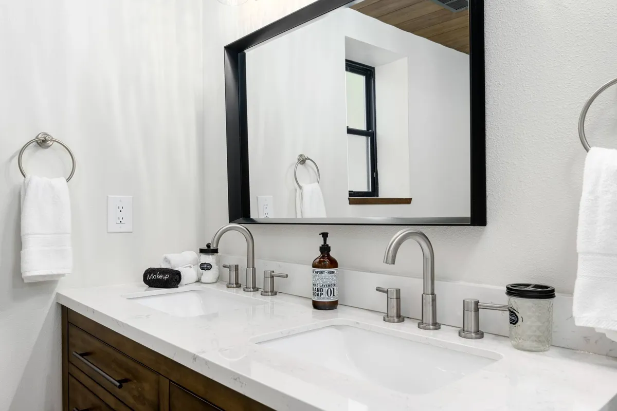 A bathroom with a double sink, elegant mirrors, and neatly arranged towels, exuding an inviting and spa-like ambiance. Subtle decor and soft lighting add to the sense of relaxation.