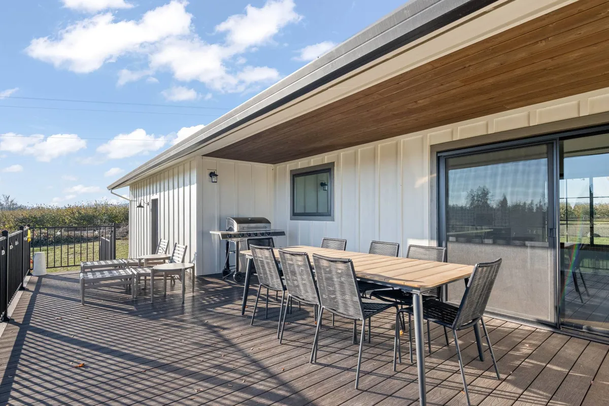 An outdoor dining area featuring a table set for a meal, a barbecue grill, reclining chairs, and a sweeping landscape view. The scene suggests casual gatherings, relaxation, and effortless connection between indoor comfort and the restorative outdoors.